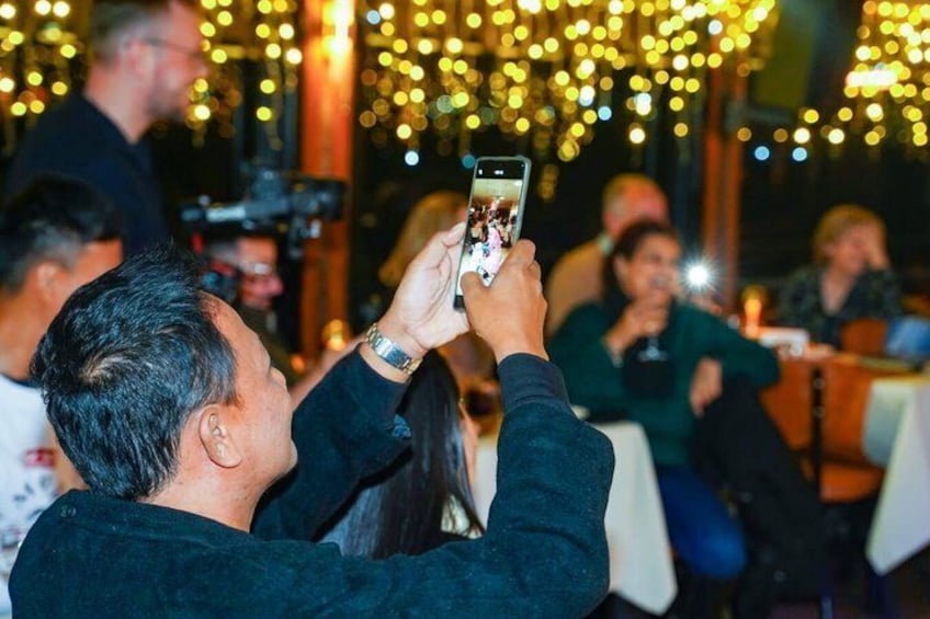 A person taking a photo with a smartphone in a dimly lit indoor setting with string lights. 2