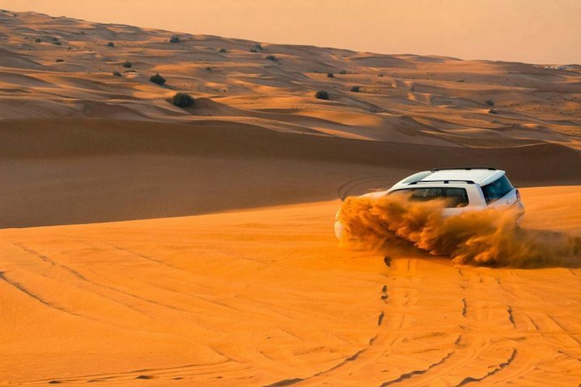 A white vehicle driving through a desert with sand dunes. 4