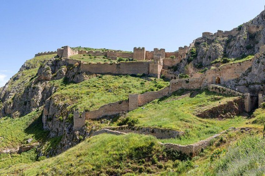 Una fortaleza de piedra histórica en una colina, con un muro amurallado y una escalera que conduce a ella. 2