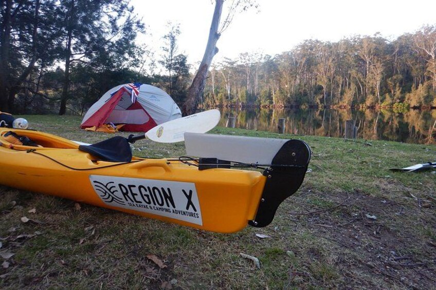 A yellow kayak with a paddle and a tent on a grassy area near a lake. 2