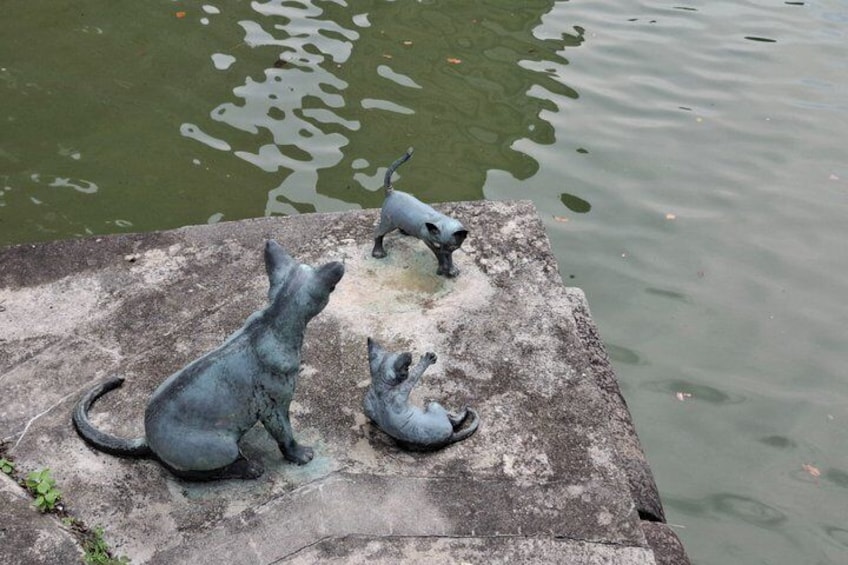 A stone structure with three bronze cat statues overlooking a body of water. 4