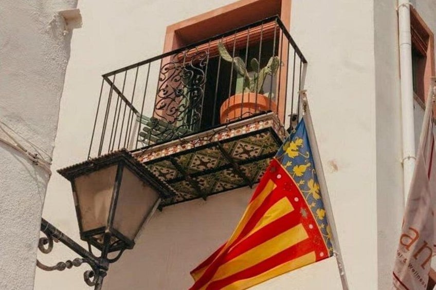 Un balcón con una maceta, un farol y una bandera. 2