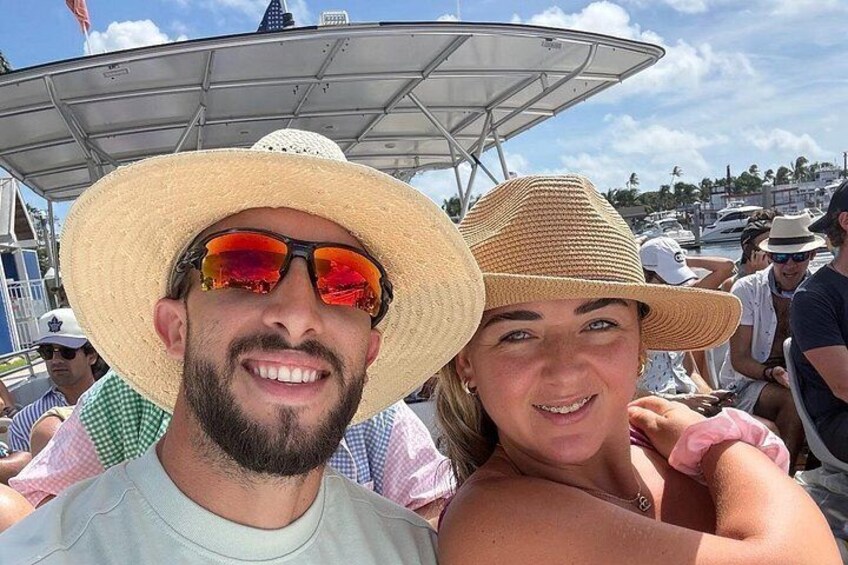 Two people wearing straw hats, one with sunglasses, on a boat with other people in the background. 4