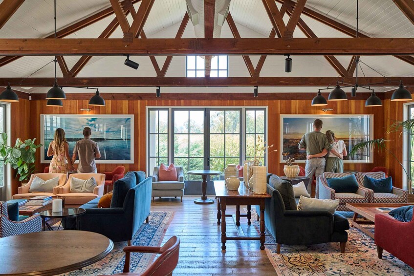 A spacious room with wooden beams, large windows, and various seating arrangements including sofas and chairs. 2