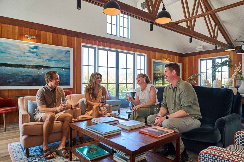 A group of people in a wooden-paneled room with large windows, a painting, and books on a table. 5
