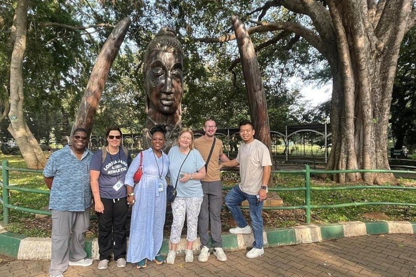 Un grupo de personas posando frente a una gran estatua con dos troncos de árbol enormes. 3