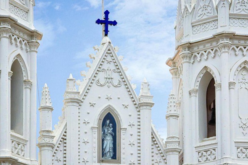 Una iglesia blanca con detallada arquitectura gótica, una cruz destacada y una estatua de una figura religiosa. 4