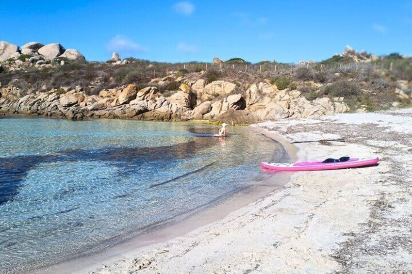 Une plage de sable fin, un kayak rose, des collines rocheuses et une personne dans l’eau. 2