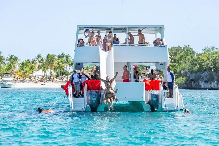 Un bote blanco con gente en la cubierta y una persona en un chaleco salvavidas rojo en el agua. 2