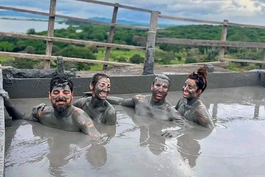 Un grupo de personas en un manantial termal, con barandilla de madera y paisaje verde al fondo. 3