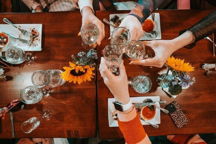 A group of people toasting with wine glasses at a wooden table with floral centerpieces. 1