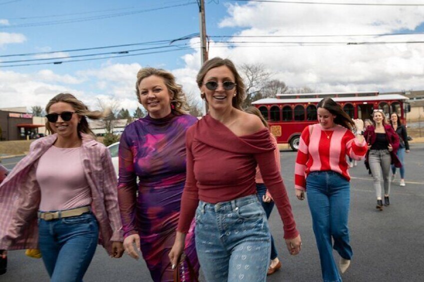 Four women walking on a street with a red bus in the background. 2