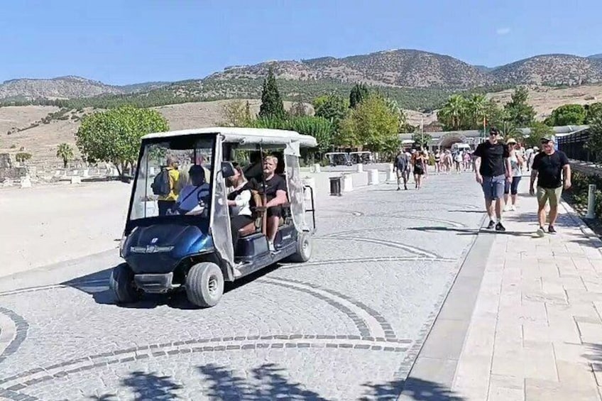 A golf cart on a paved path with people walking in the background and a mountainous landscape. 2