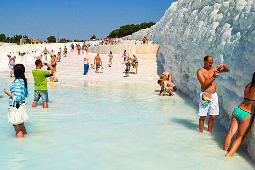 A crowded beach with people in the water and a large ice formation. 5