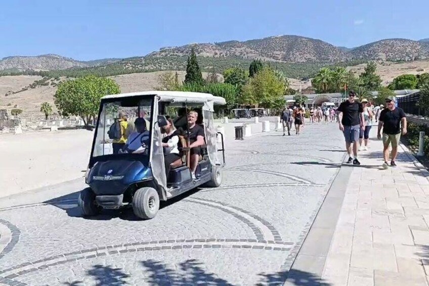 A golf cart on a paved path with people walking in the background and mountains in the distance. 2