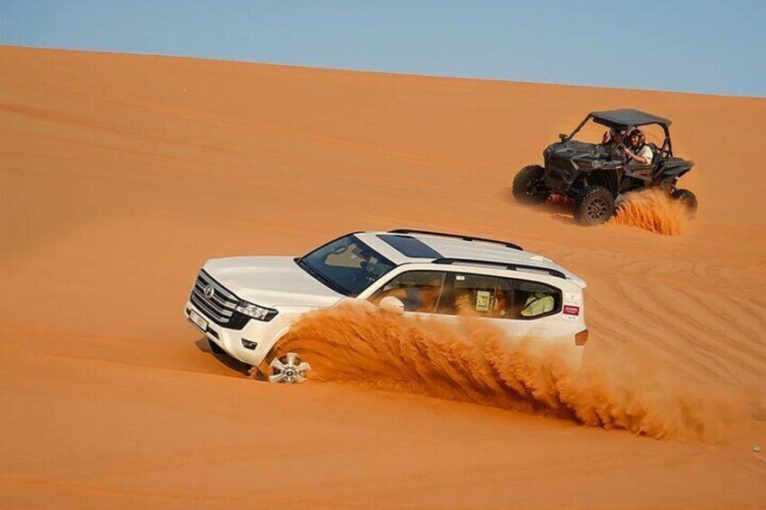 A white SUV driving through a desert with sand being kicked up behind it. 1