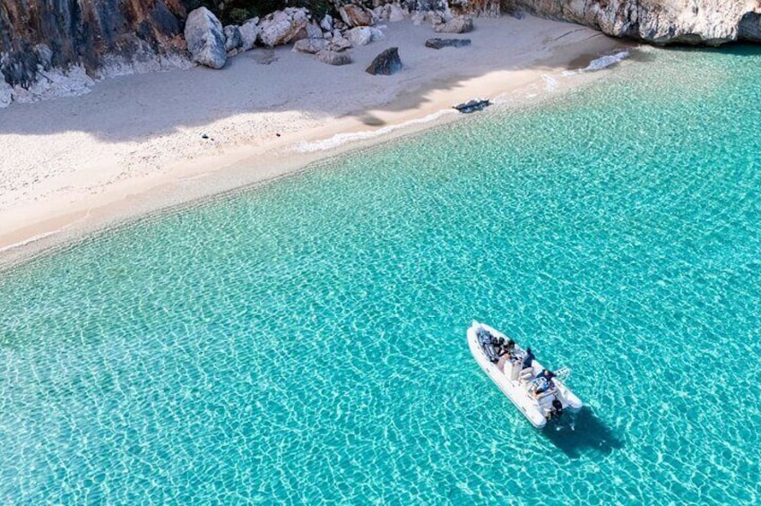 Een boot op een heldere turquoise zee, met een zandstrand en rotsachtige kliffen op de achtergrond. 2