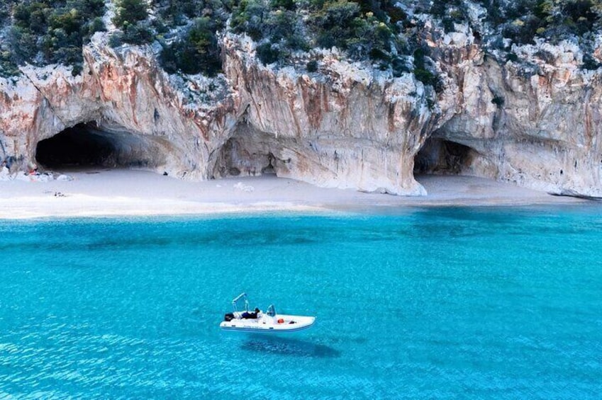 Een boot op turquoise water nabij een rotsachtige klif met grotten. 4