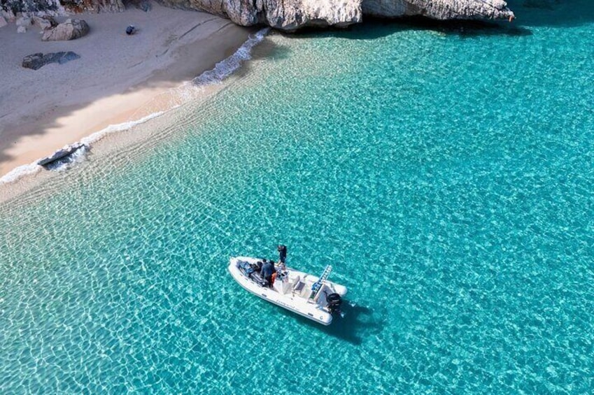 Een boot op helder turquoise water nabij een zandstrand met rotsformaties. 3