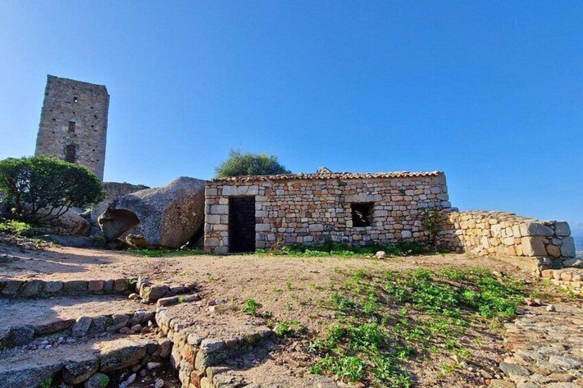Un edificio de piedra con una puerta, una gran formación rocosa y una torre al fondo. 3