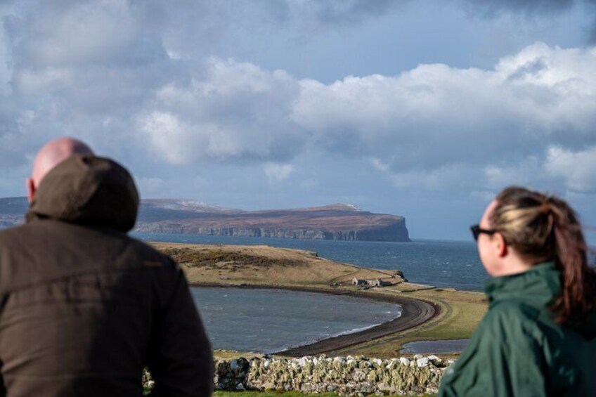A coastal landscape with a cliff, a curving shoreline, and a stone wall. 4