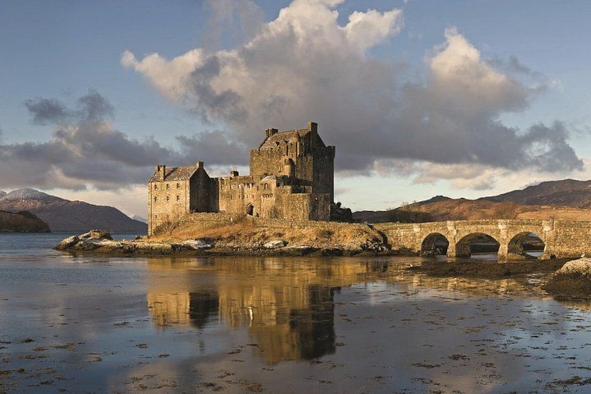 A historic castle by a calm lake with a stone bridge. 2