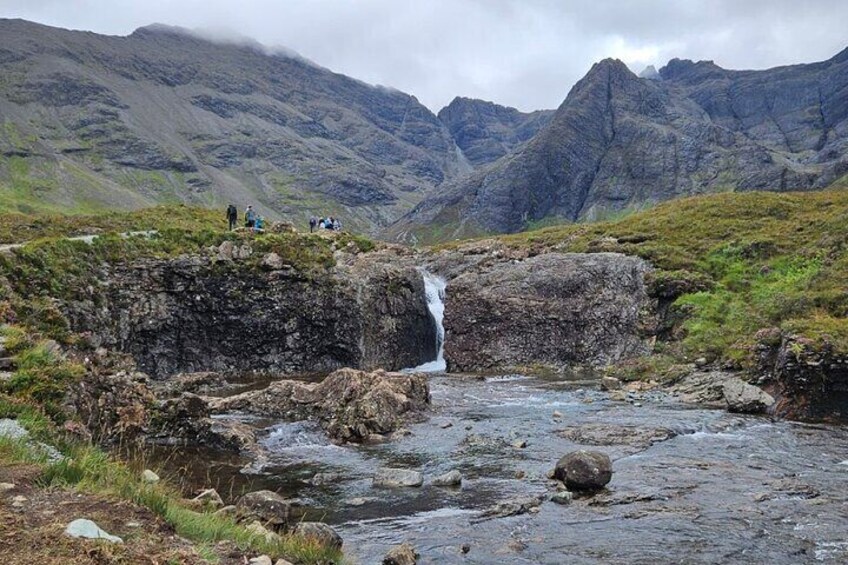 A waterfall in a mountainous area with rocky terrain and a few people observing it. 3