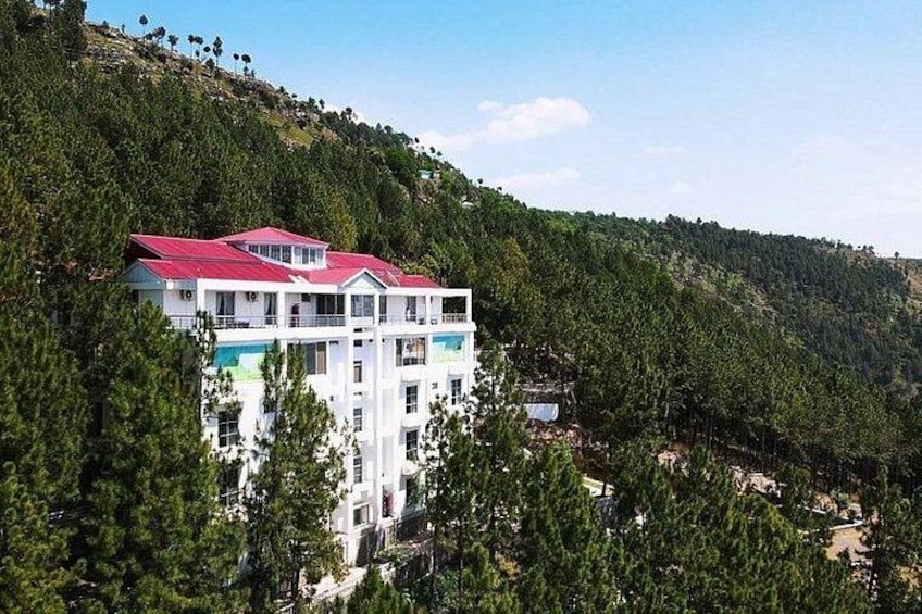A multi-story building with a red roof, surrounded by dense forest and hills. 5