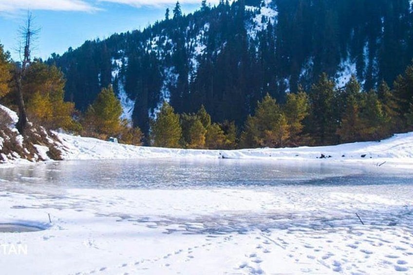 A frozen lake surrounded by trees and mountains. 3