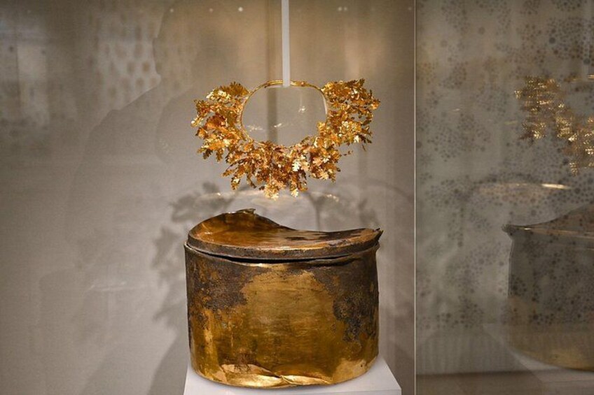 Un artefacto dorado con diseño floral, exhibido en una vitrina. 3