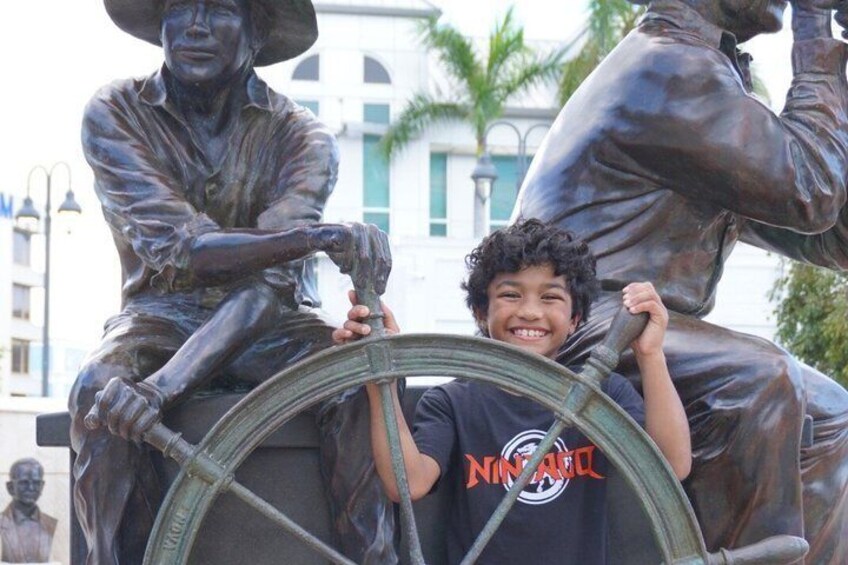 Une statue de bronze représentant un homme tenant une roue, un enfant tenant également la roue, et une autre statue en arrière-plan. 1