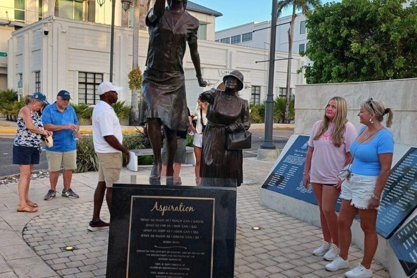 Une statue de bronze représentant une femme tenant un livre, entourée d’une foule. 4