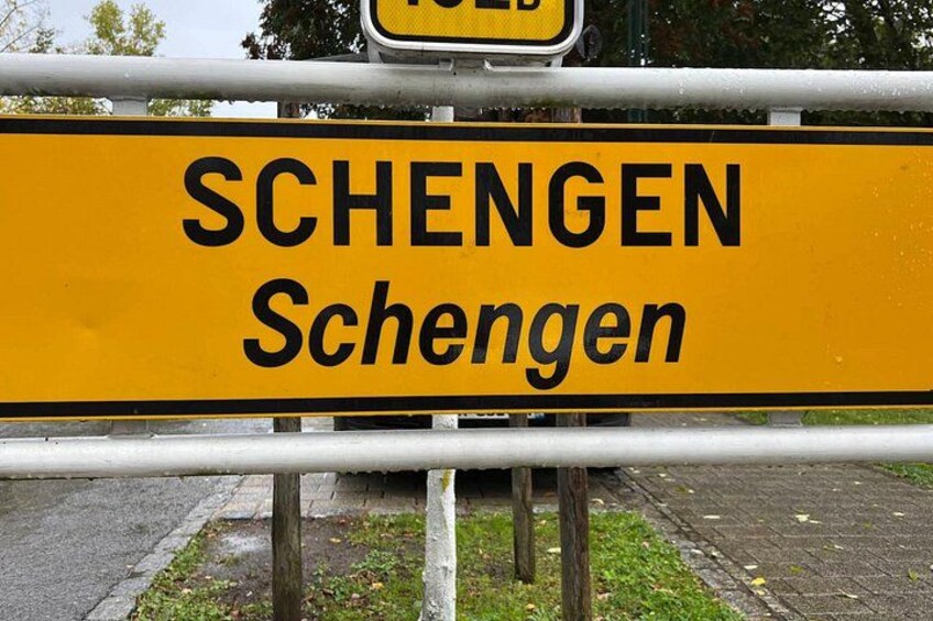 A yellow street sign with the word 'SCHENGEN' and its English translation. 3