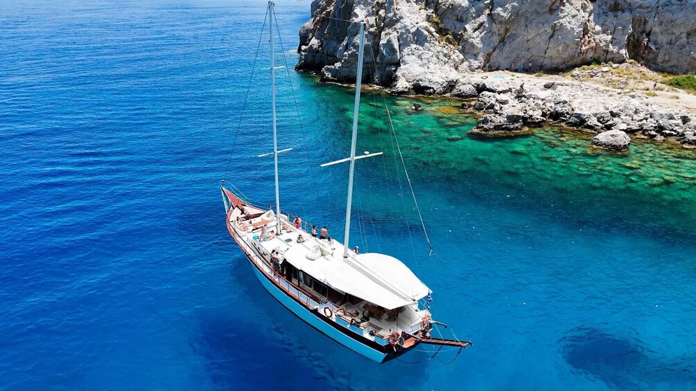A sailboat on a clear blue sea with rocky coastline. 1