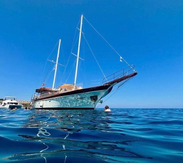 A sailboat named 'Azzurra K' anchored in clear blue waters with a person swimming nearby. 4