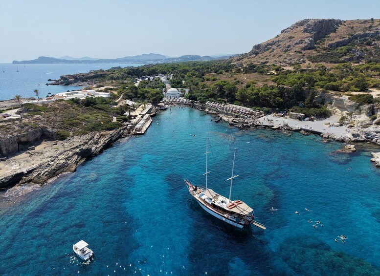 A coastal area with clear blue waters, a large boat anchored near the shore, and a rocky landscape with sparse vegetation. 2