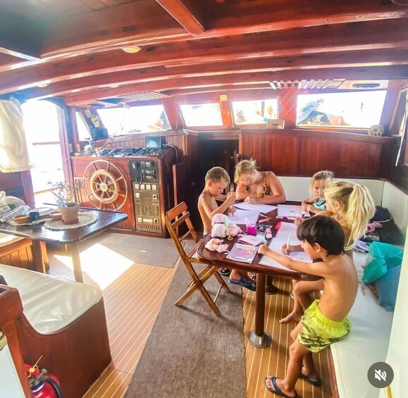 A group of children sitting at a table, engaged in drawing or writing activities on a boat. 2