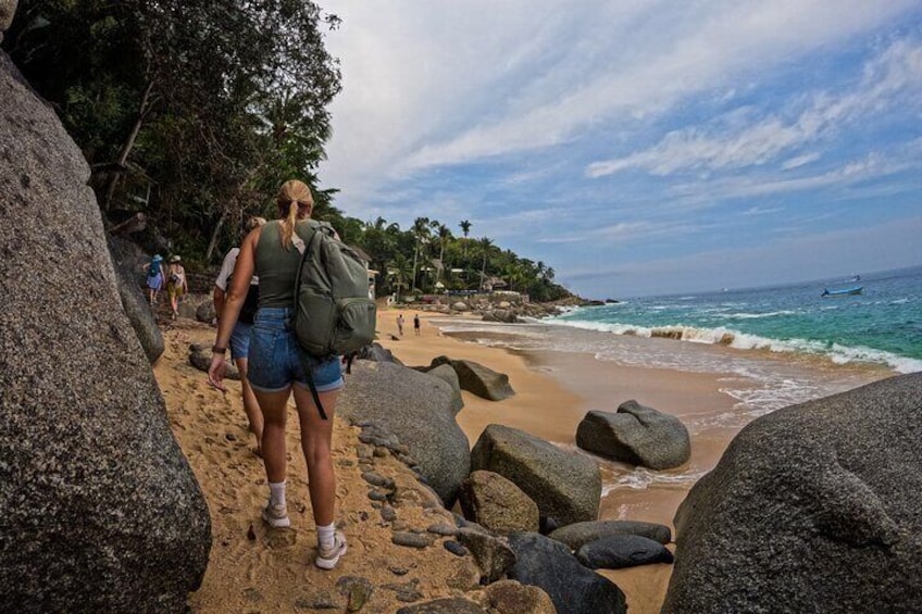 A beach with large rocks, a person with a backpack, and the ocean in the background. 5