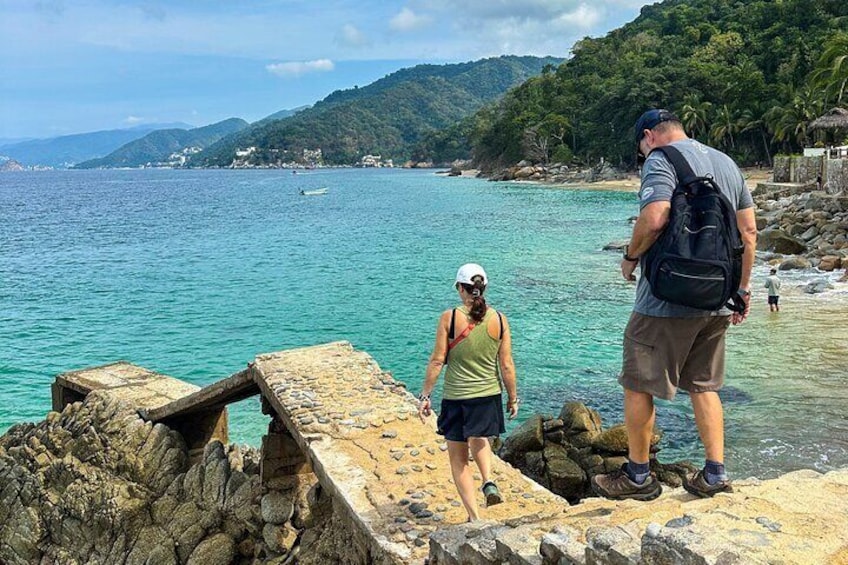 A rocky shoreline with a person standing on a stone platform overlooking turquoise waters. 1