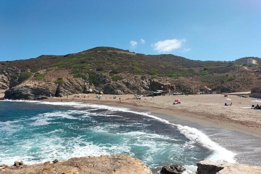 Ein Küstenstrand mit brechenden Wellen, sandigem Ufer und felsigen Klippen im Hintergrund. 4