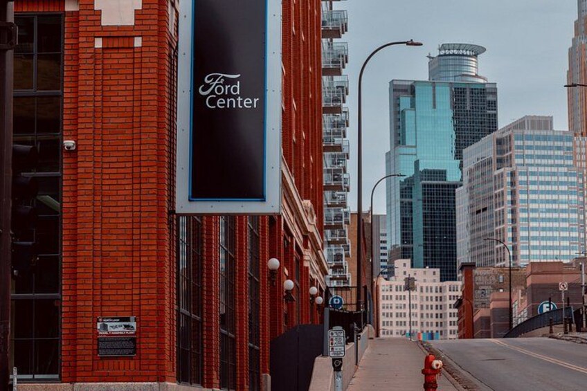 Ein roter Backsteinbau mit einem Schild ‚Ford Center‘, einem Hydranten und modernen Wolkenkratzern im Hintergrund. 3