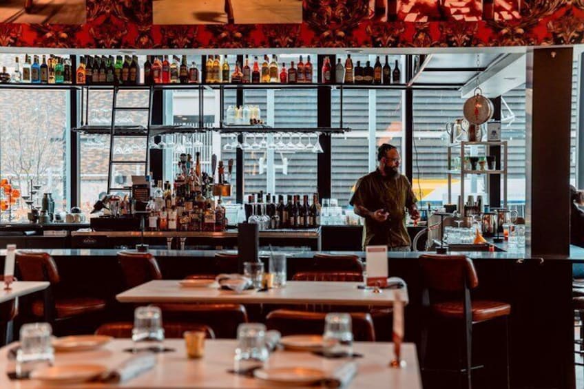 A bar with multiple tables and chairs, a bartender, and shelves stocked with bottles. 5