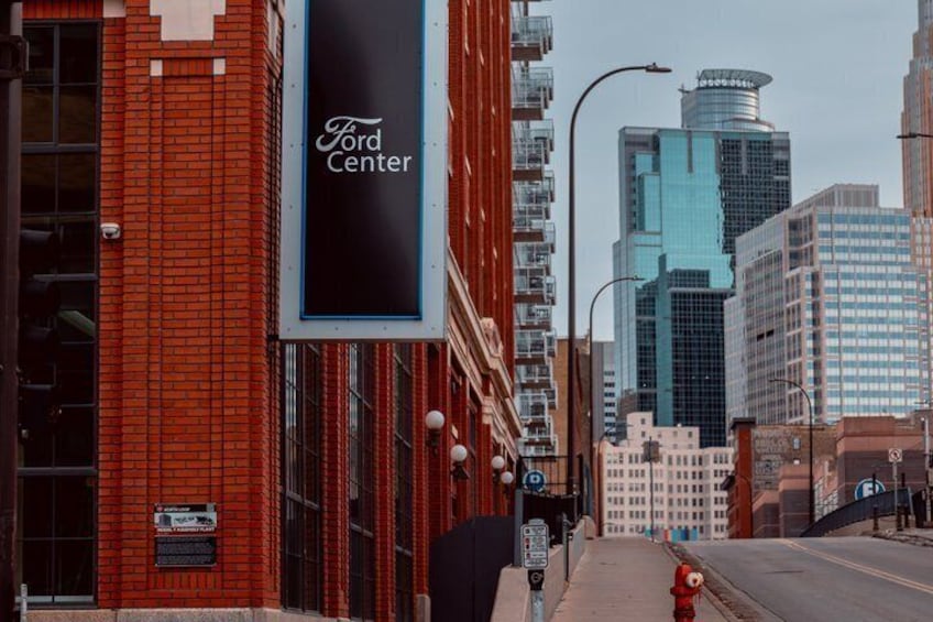 A red brick building with a Ford Center sign, a fire hydrant, and tall buildings in the background. 2