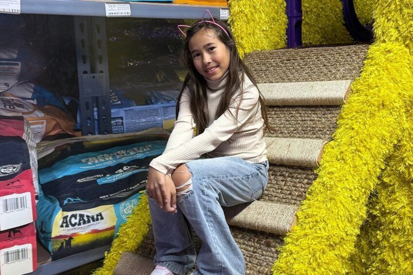 A person sitting on a staircase with yellow fluffy decorations, surrounded by shelves with various items. 3