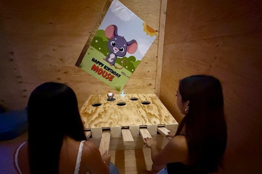 Two people playing a wooden board game with a mouse-themed birthday card on the wall. 1
