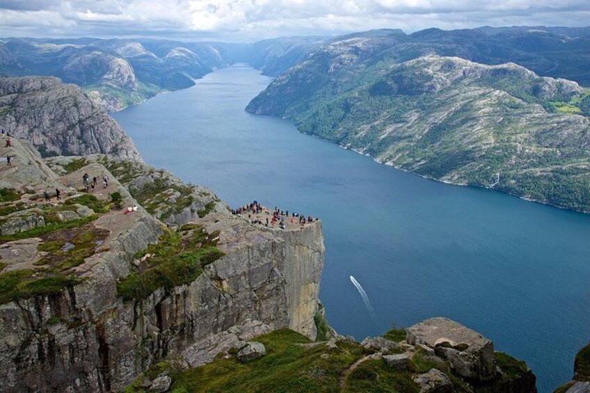 A fjord with a steep cliff, a waterfall, and a group of people on the cliff edge. 4