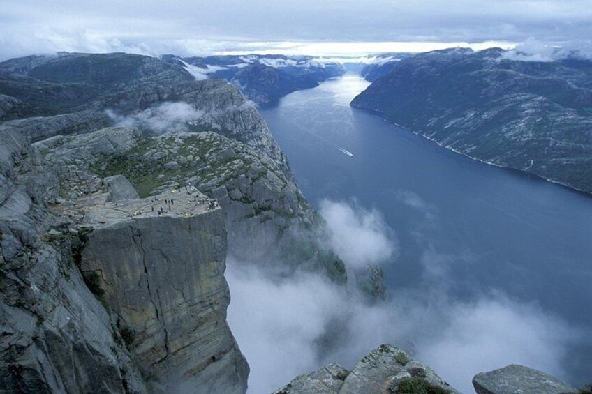 A mountainous landscape with a lake, a rocky cliff, and a small group of people at the cliff's edge. 5