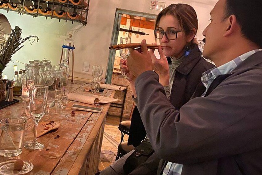 A person playing a flute at a wooden table with wine glasses and bottles. 5