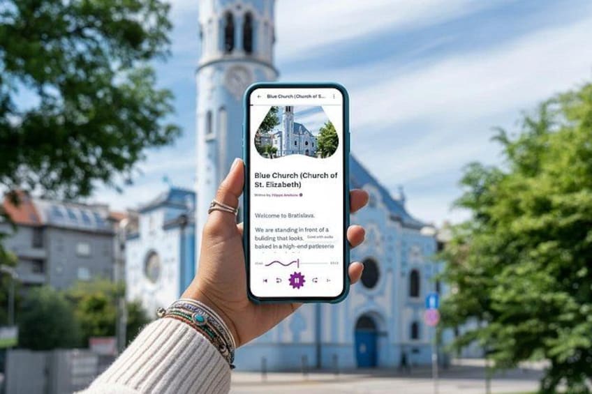 En hand håller en smartphone som visar en app för kyrkor, och i bakgrunden syns en kyrkobyggnad. 1