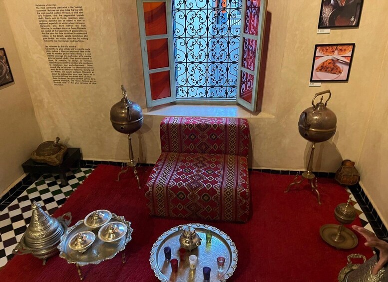 A traditional Moroccan room with a patterned sofa, ornate metal tea set, and a decorative window. 2